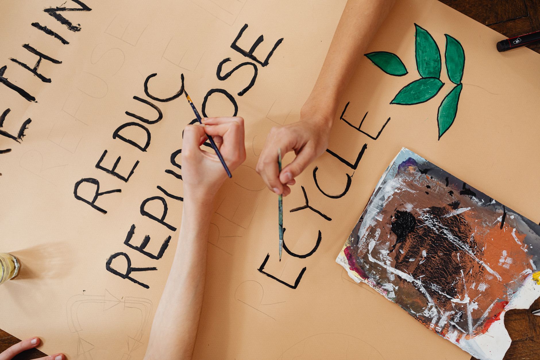 Hands painting sustainability message poster emphasizing recycling and repurposing.