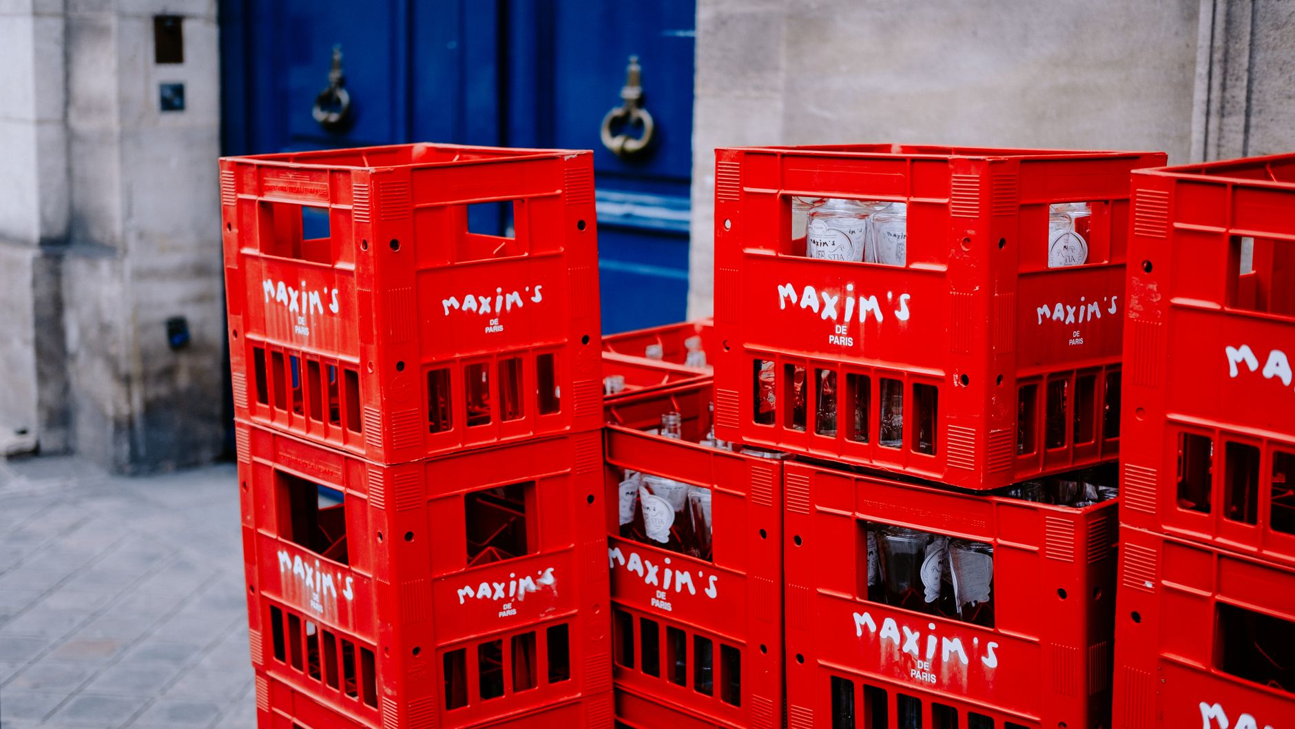 Red Maxim's de Paris crates stacked on a sidewalk, showcasing Parisian street scene.