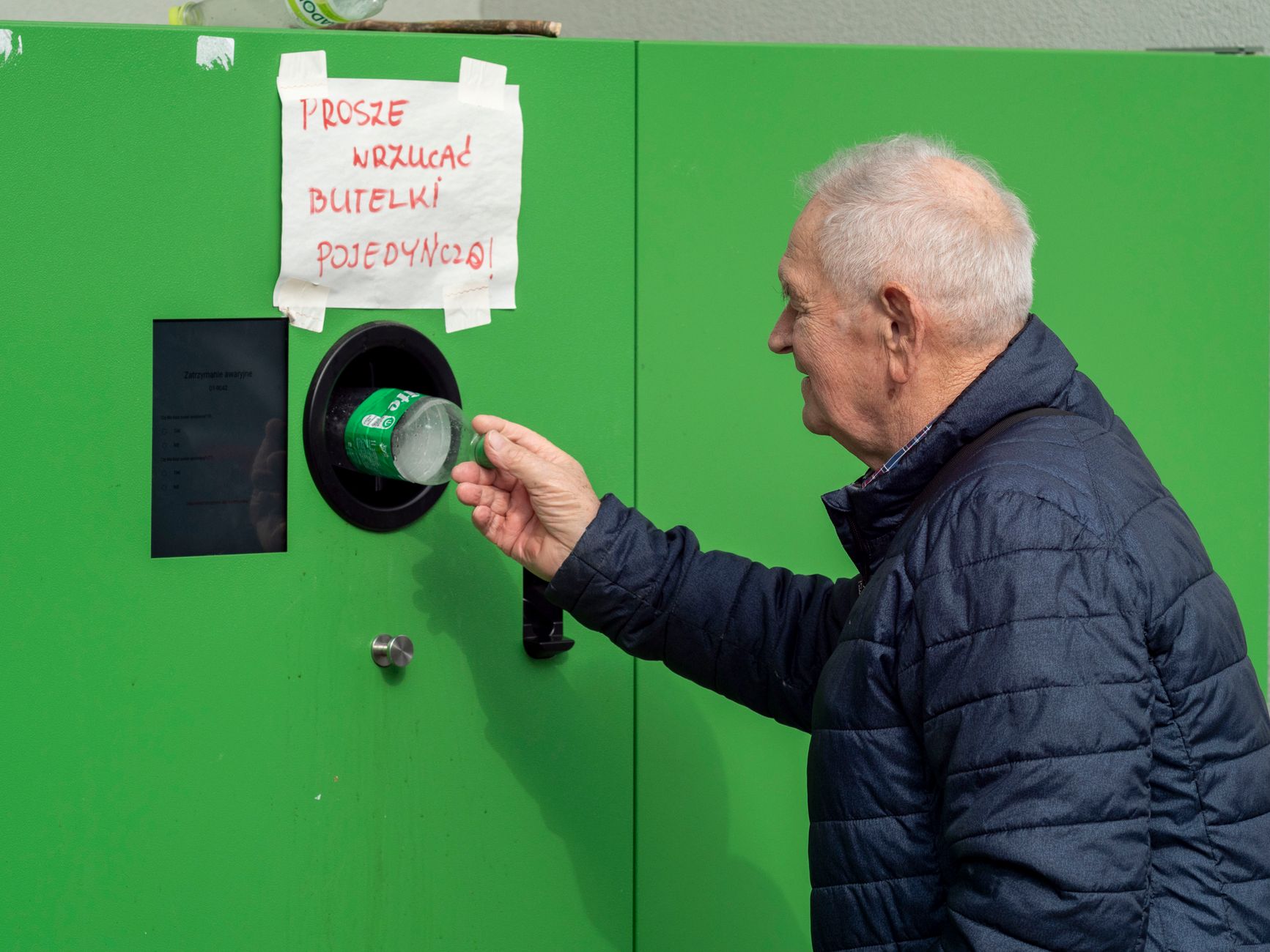 An elderly man recycles a bottle in Wrocław, Poland, promoting environmental responsibility.