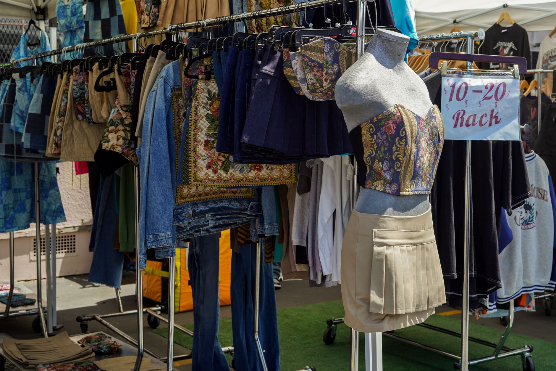 A colorful display of secondhand clothing at a Los Angeles flea market, featuring denim, skirts, and a mannequin.