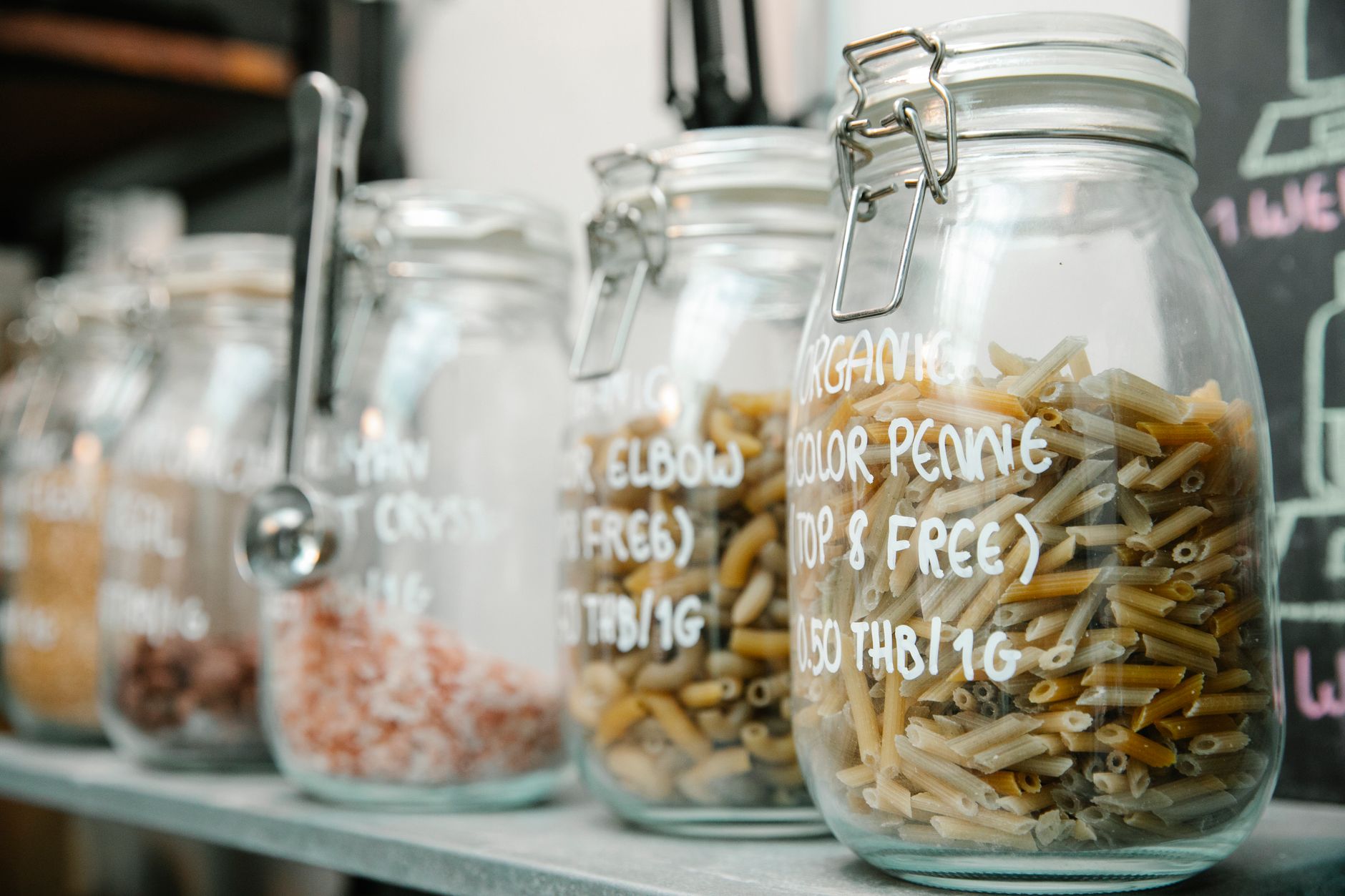 Set of glass jars with lid containing penne and elbow macaroni and various products on wooden shelf