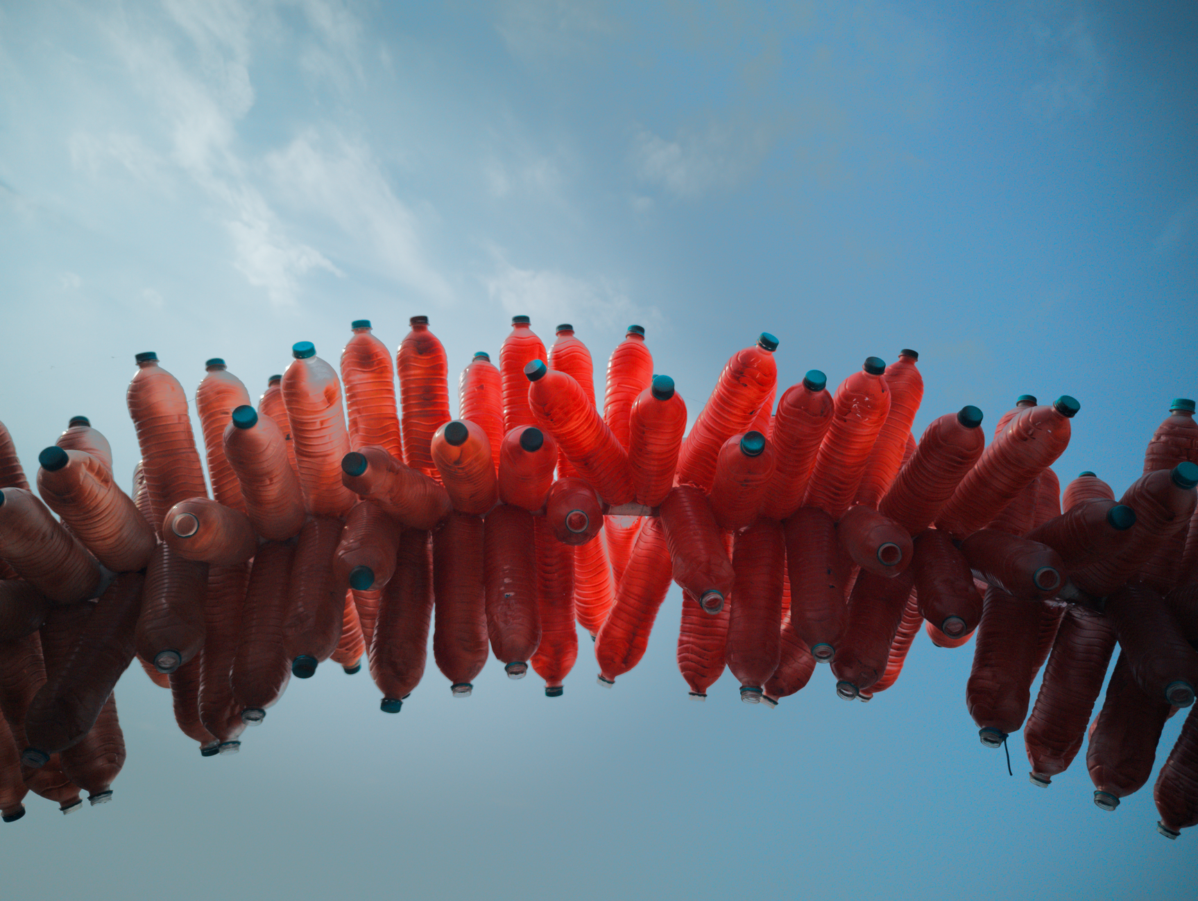 Colorful upcycled plastic bottle art against a clear blue sky inspires eco-friendly creativity.