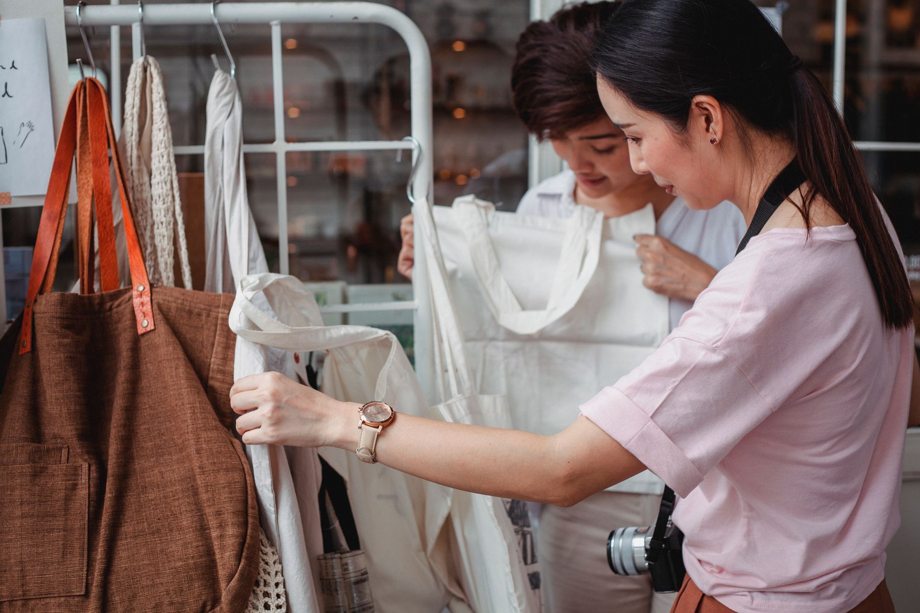 Side view of fashionable young ethnic female friends choosing stylish eco friendly cotton bags in boutique