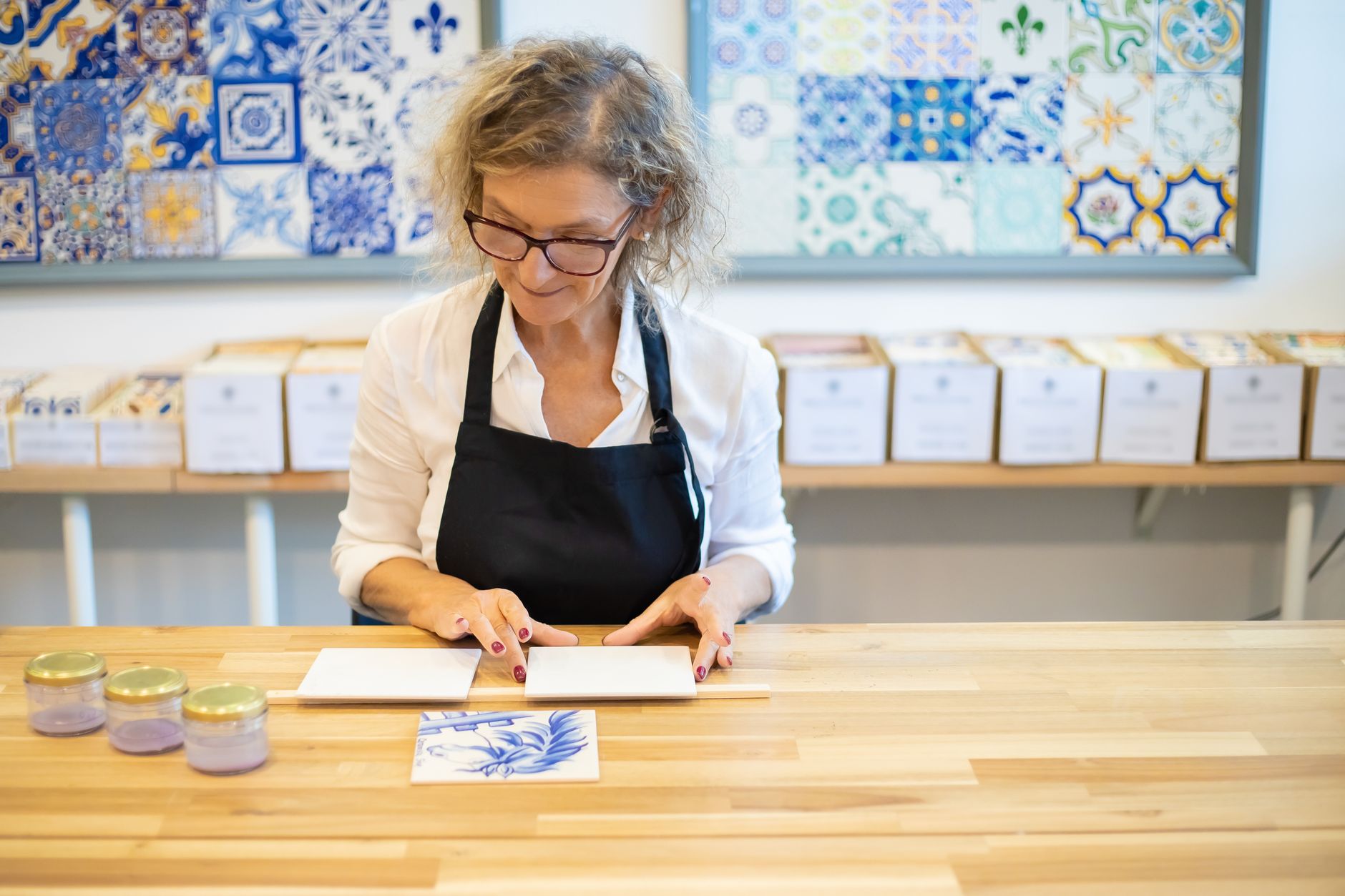 Woman in workshop creating decorative Portuguese tiles, featuring intricate blue patterns.