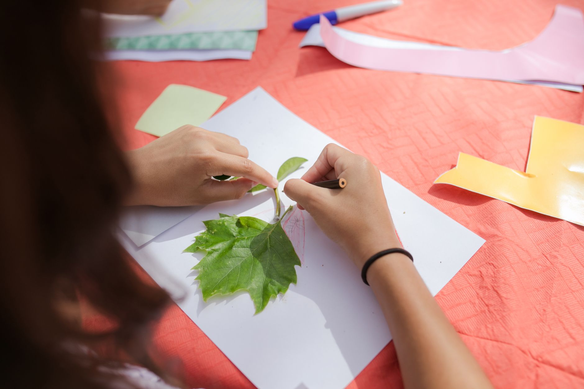 Hands engage in leaf tracing on paper, capturing nature's beauty in an art activity.