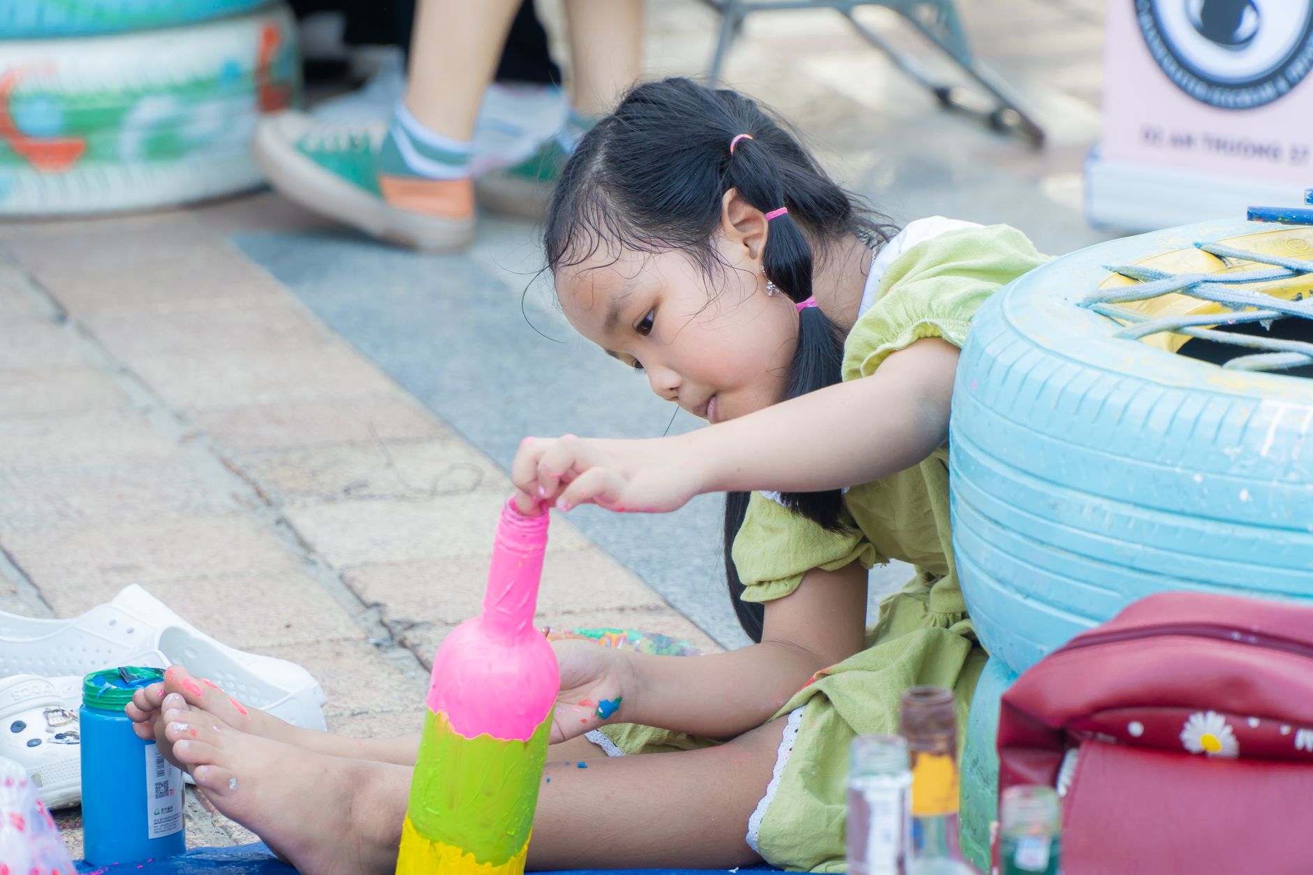 A young girl engaging in creative bottle painting art outdoors, displaying focus and creativity.
