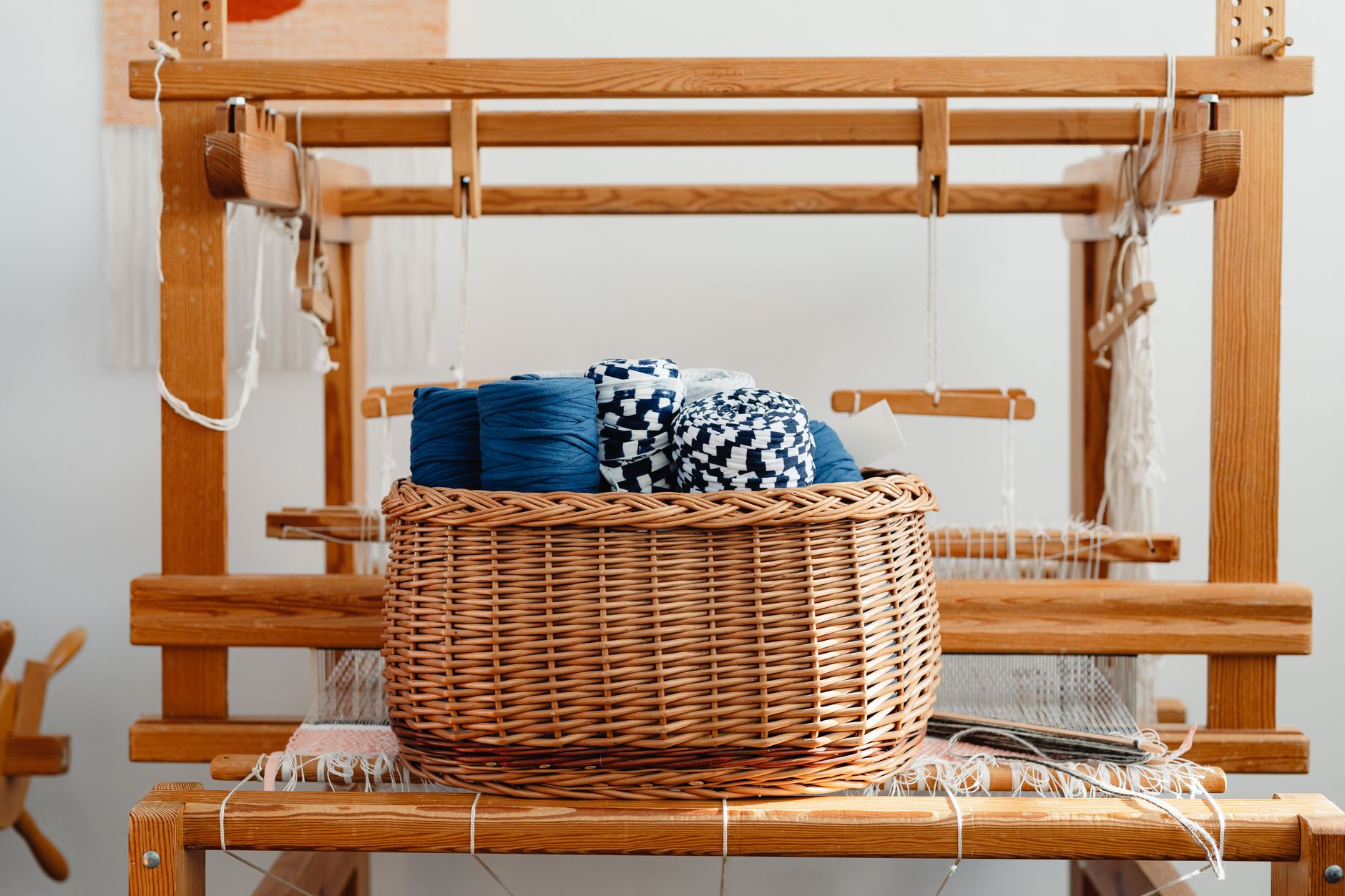 Basket filled with yarn and threads placed on a traditional wooden loom in an artisan workshop.
