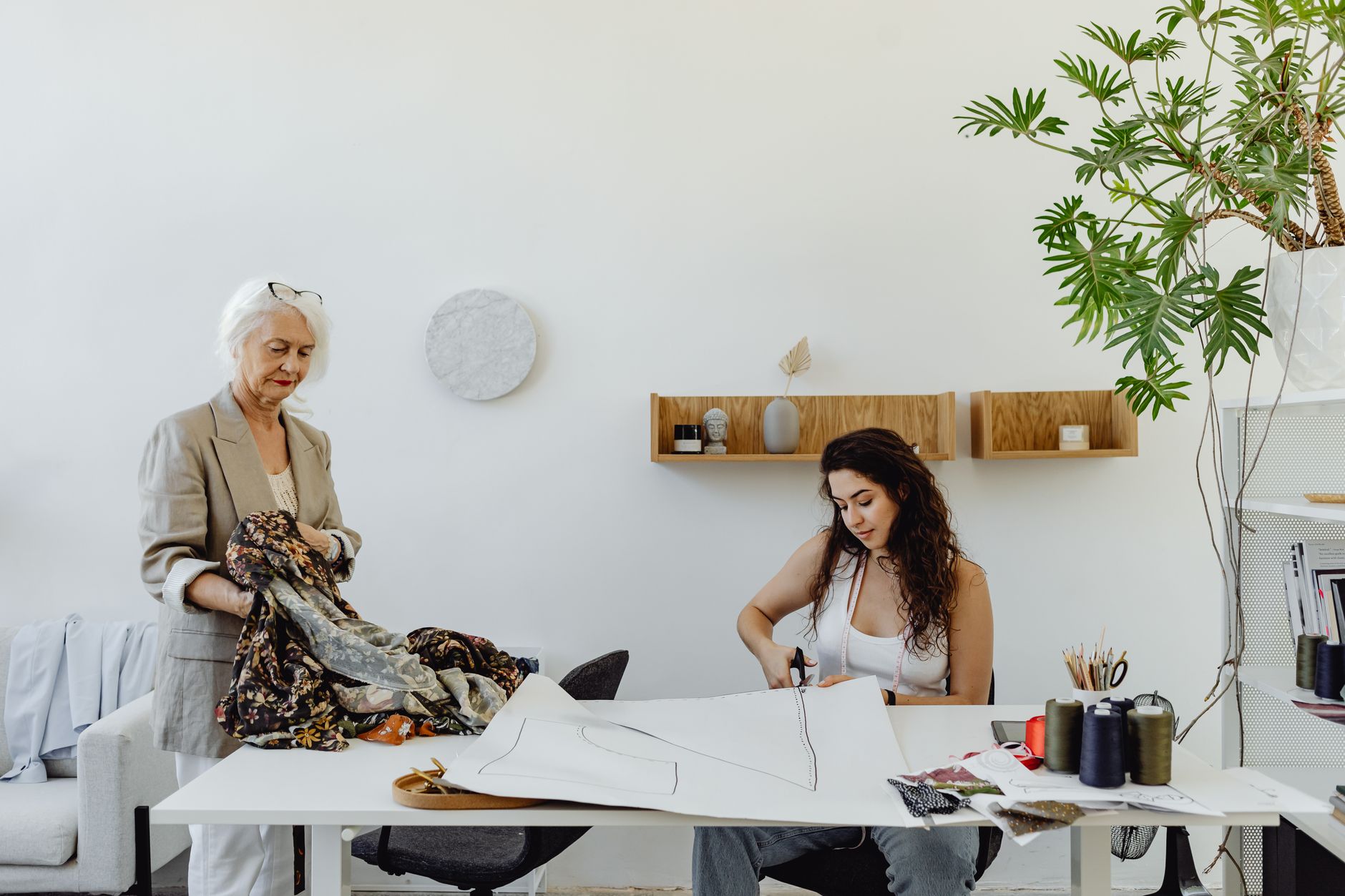Two women collaborating in a sewing studio with fabric and patterns, showcasing creativity and teamwork.