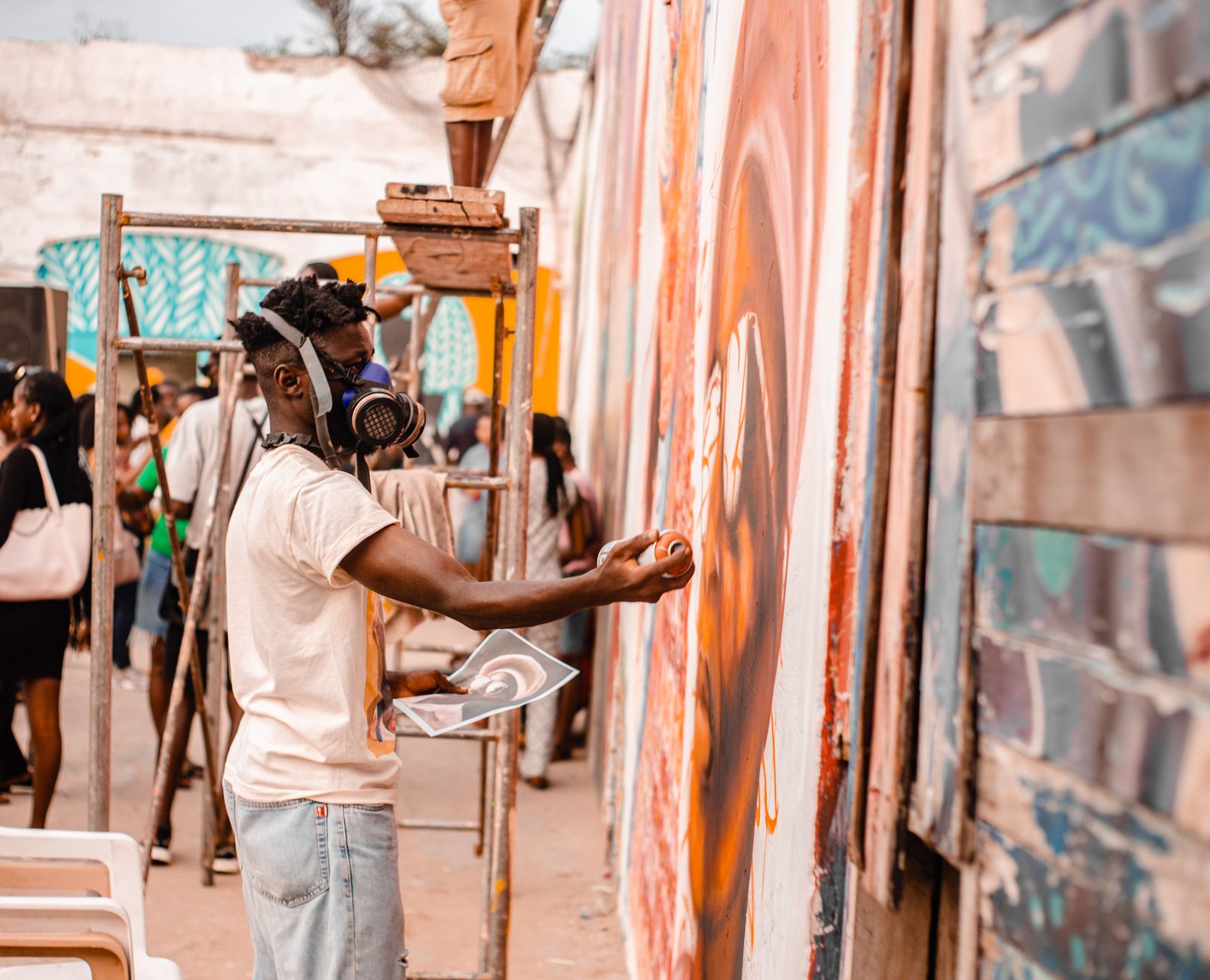 Artist spray painting a colorful mural on an outdoor wall during the day.