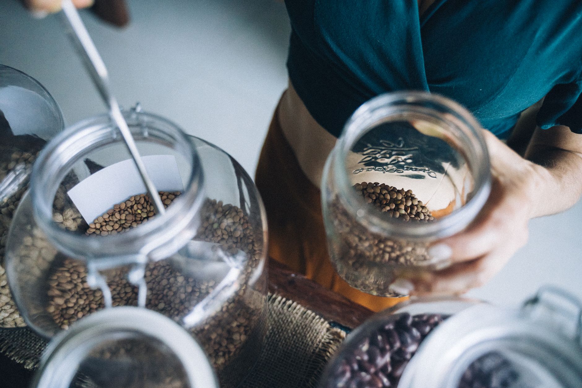 Person refilling glass jars with seeds in eco-friendly refill store.