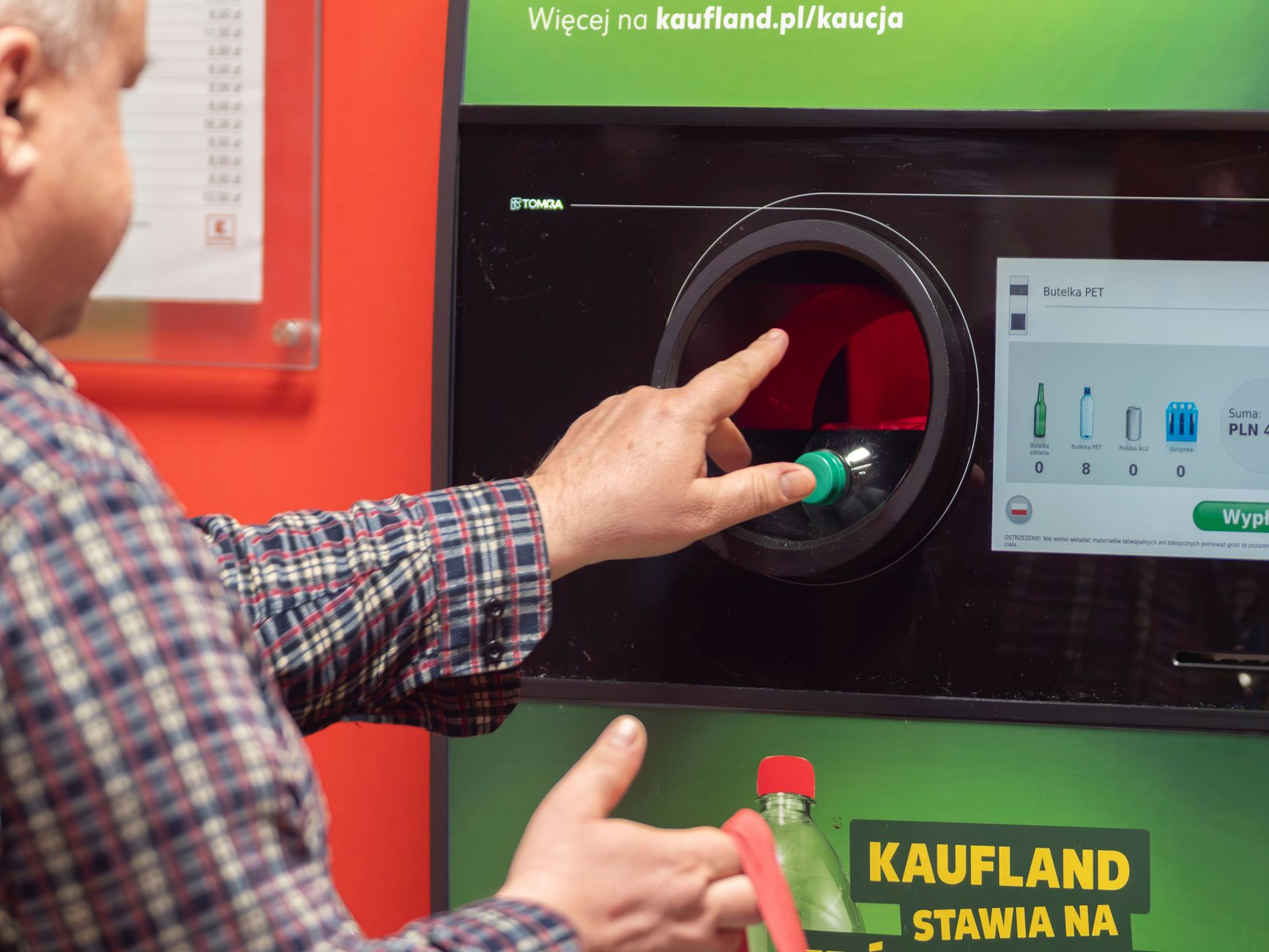 A man inserting a plastic bottle into a return machine at Kaufland in Wrocław, Poland.