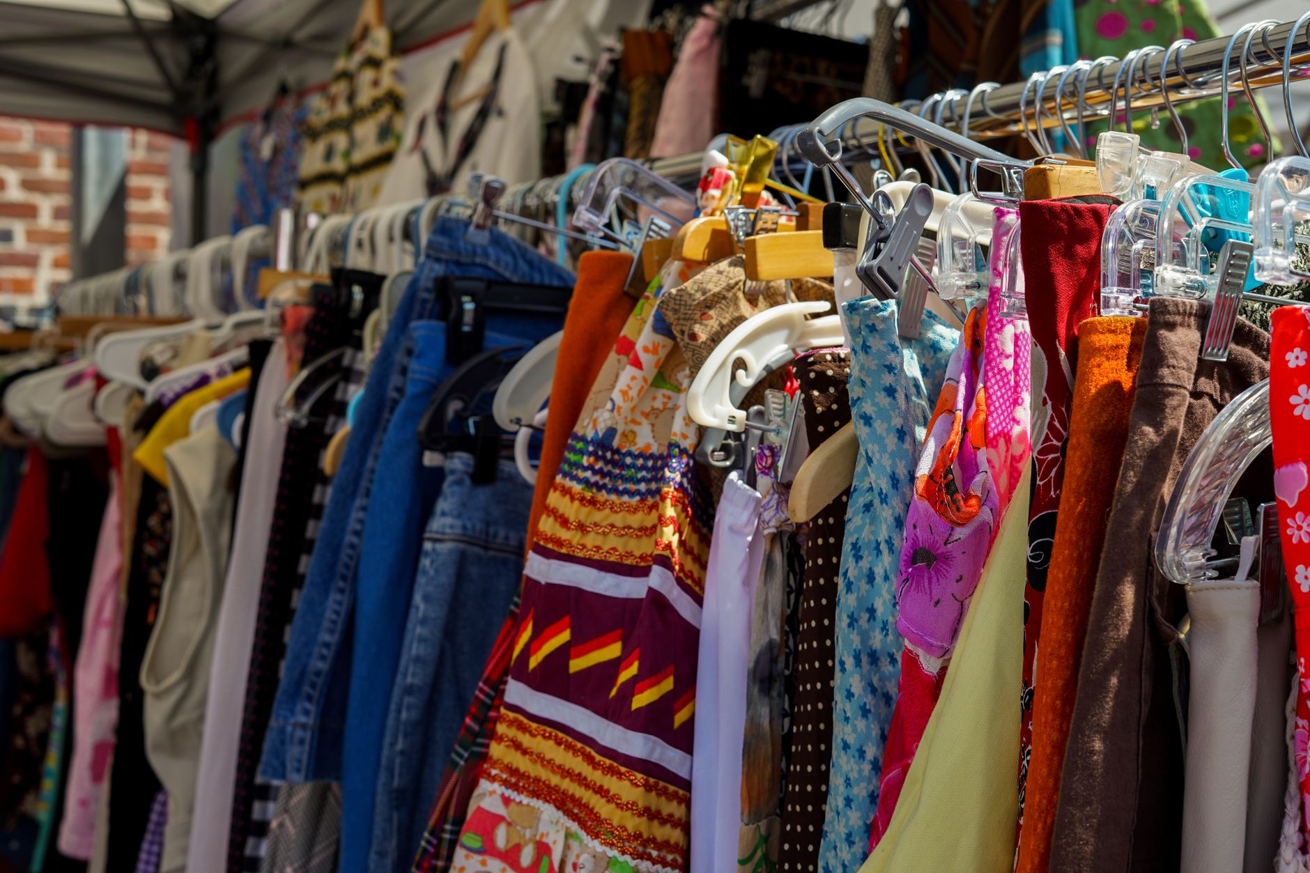 A colorful array of clothes on hangers at a bustling outdoor market.