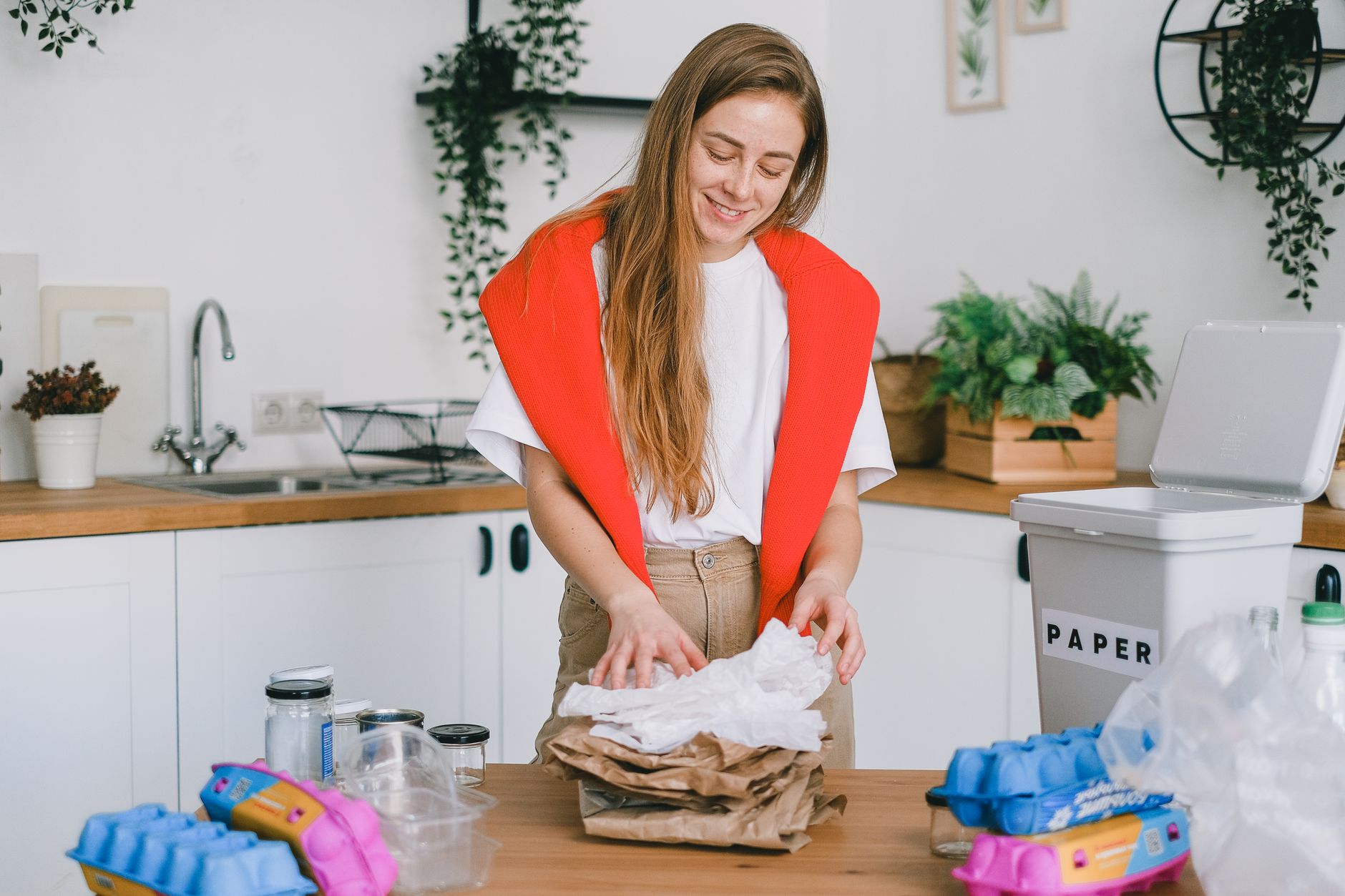 Positive female standing at table and separating paper trash from plastic glass and egg boxes