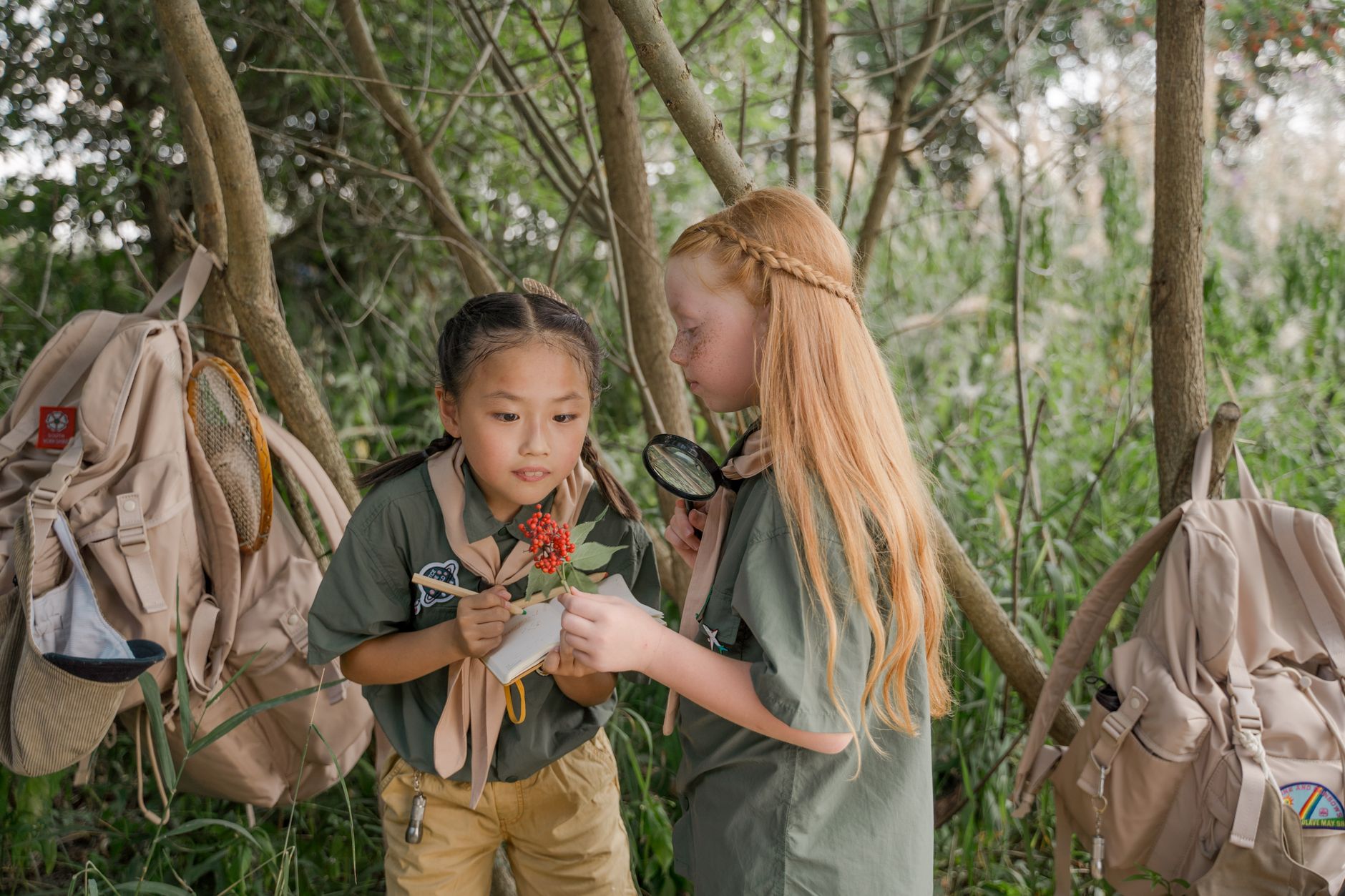 Two young girl scouts examining flora in a woodland summer camp setting.