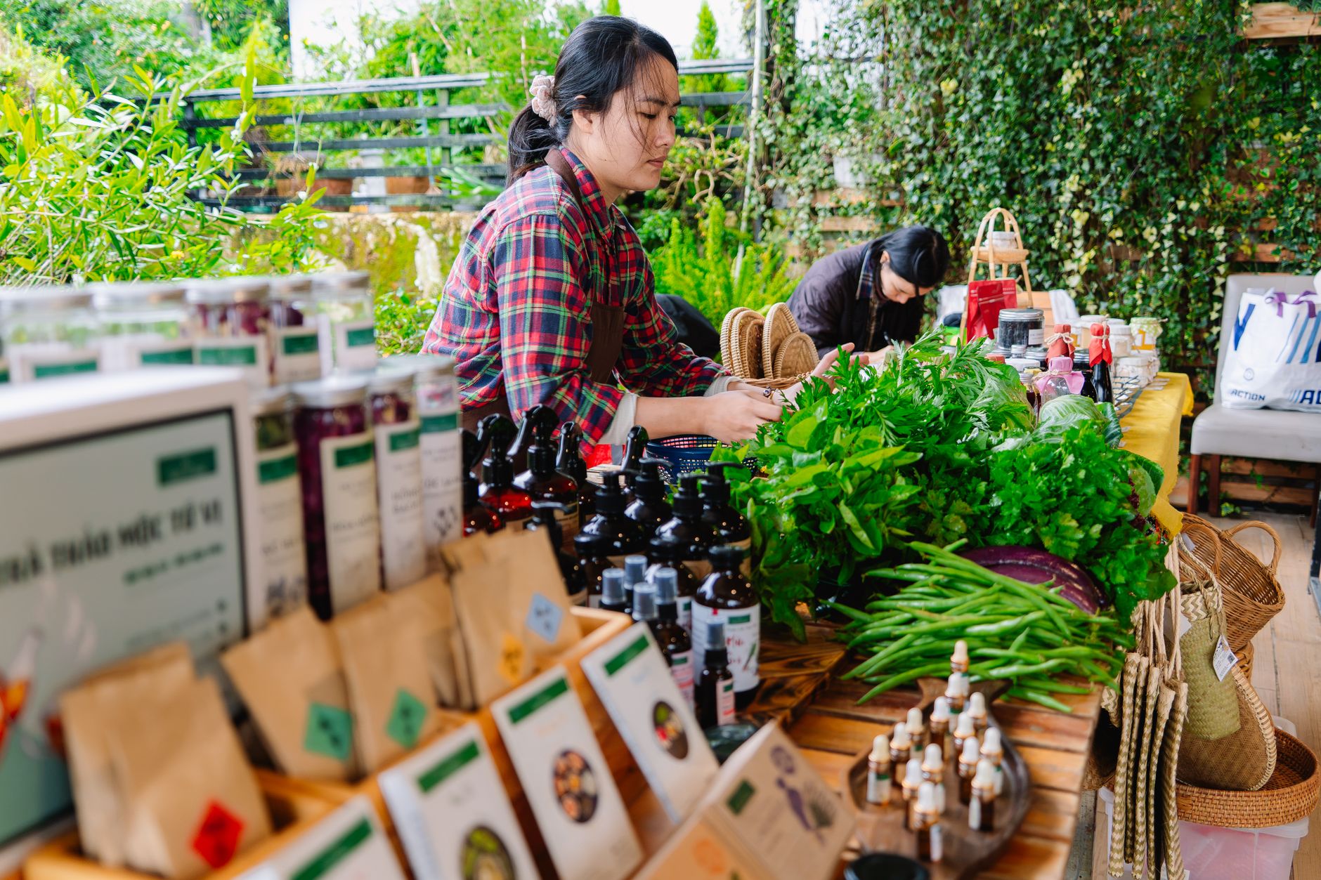 A lively scene at an outdoor market stall with women selling organic products and fresh herbs.