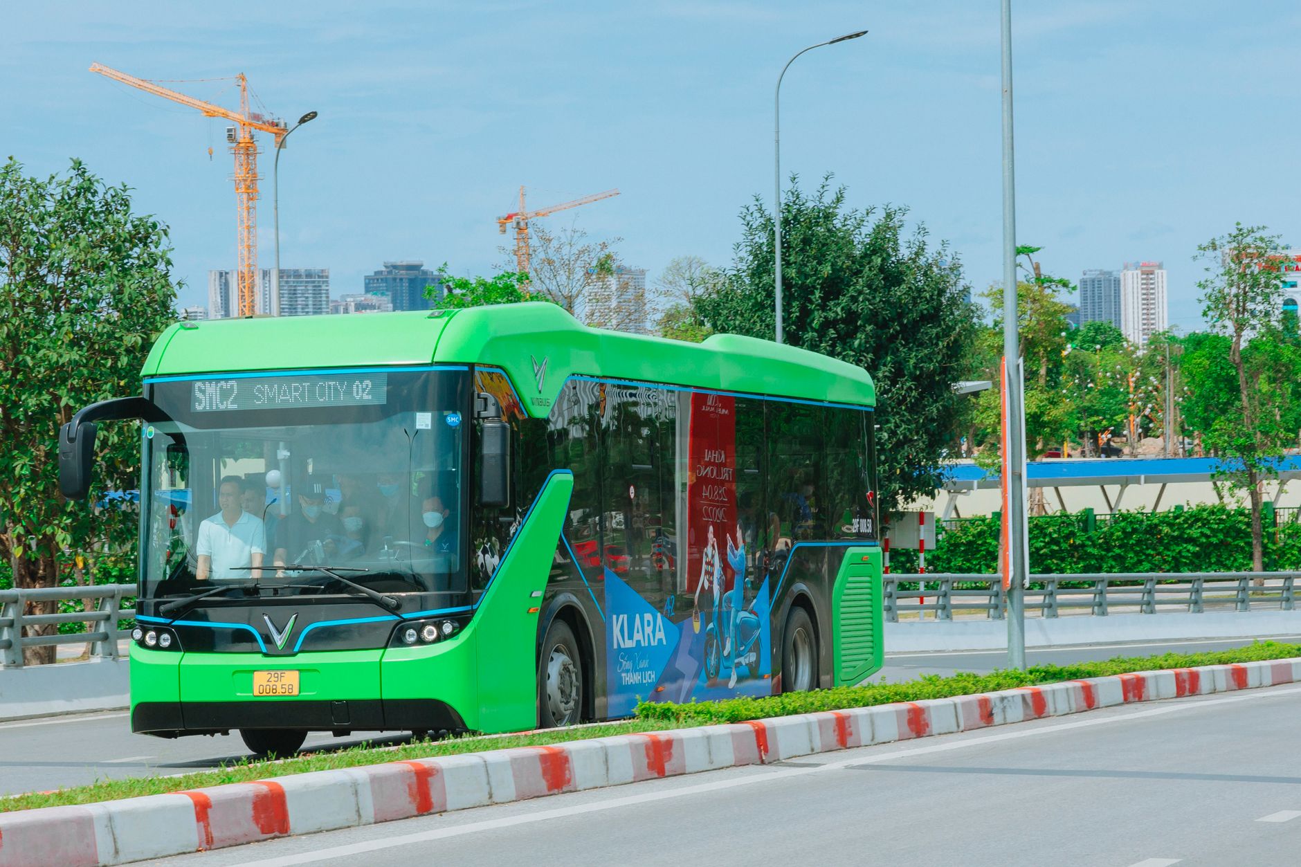 A modern green electric bus travels through Hanoi, showcasing urban transportation and city infrastructure.