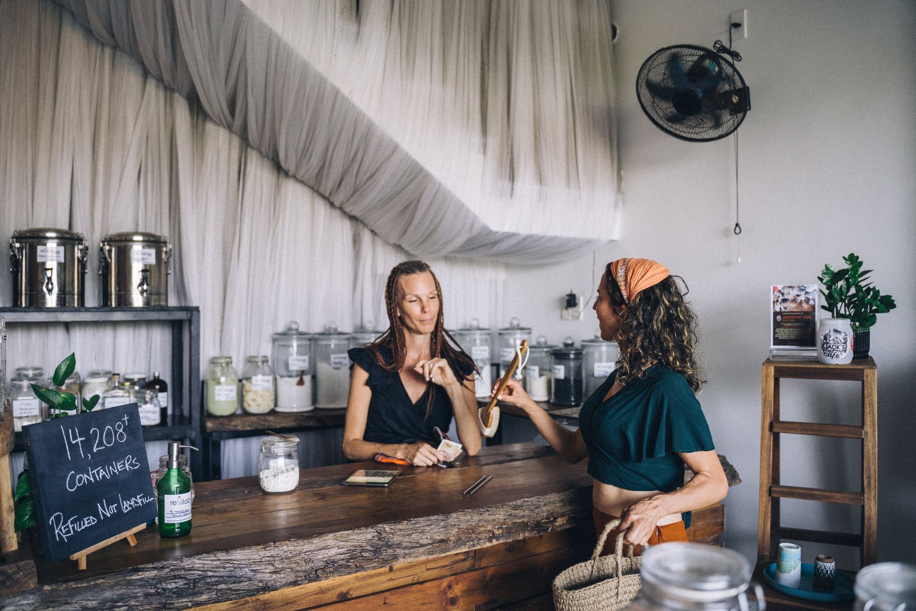 Two women shopping in an eco-friendly store with refillable glass jars and organic products.
