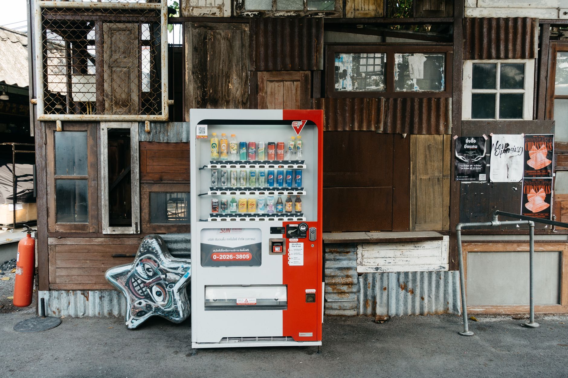 A vending machine stands in front of an eclectic wall with corrugated metal and old wood panels.