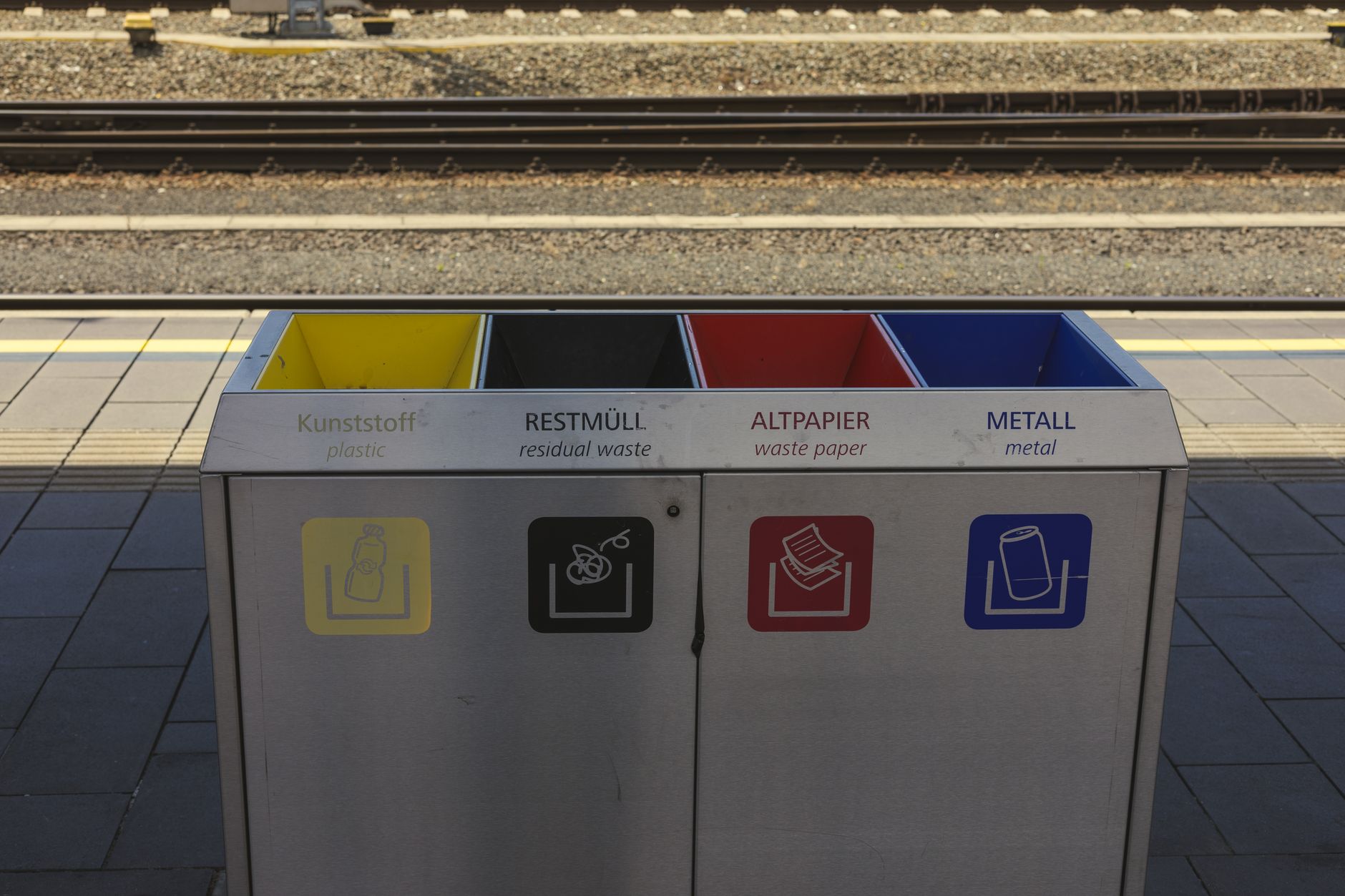 Color-coded recycling bins at a train station, promoting waste separation and environmental sustainability.