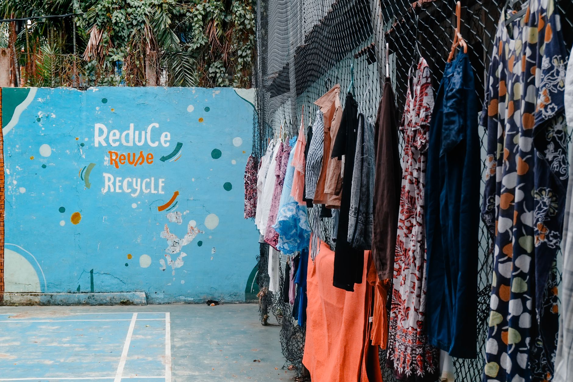 Vibrant clothing hangs beside a mural promoting recycling in Central Jakarta.