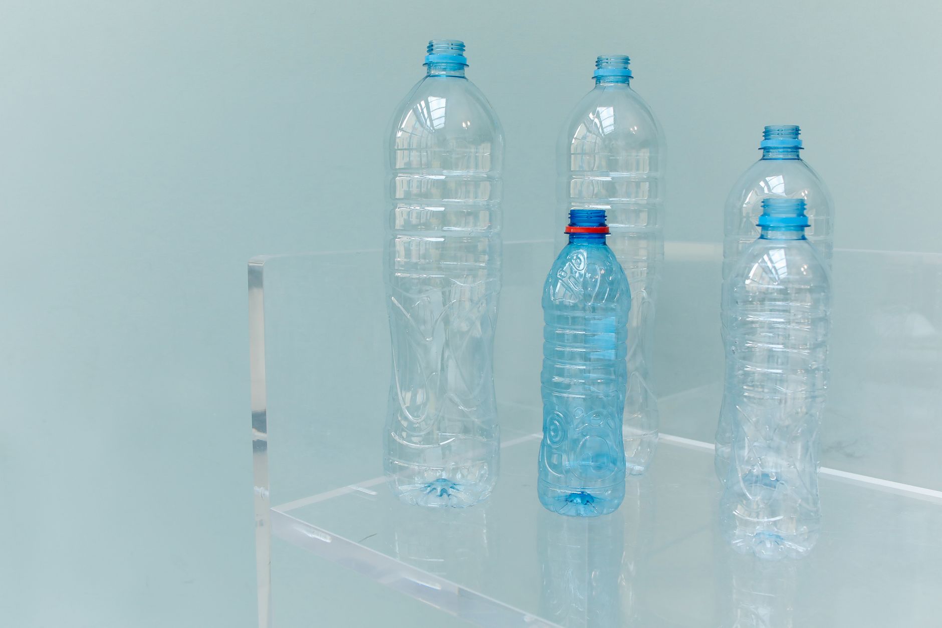 Five assorted empty plastic bottles displayed on a clear shelf with a soft blue background.