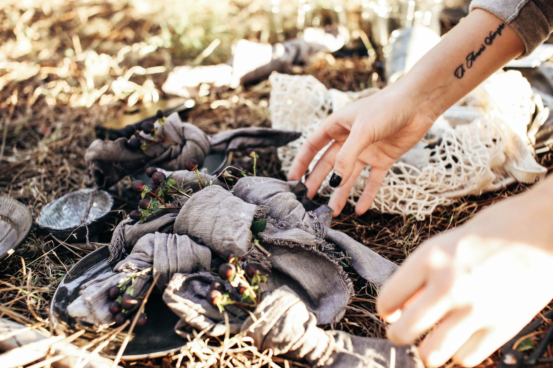 Crop faceless female setting decorative napkins with herbs on dry grassy meadow near utensil and reusable bag while having picnic in sunny d