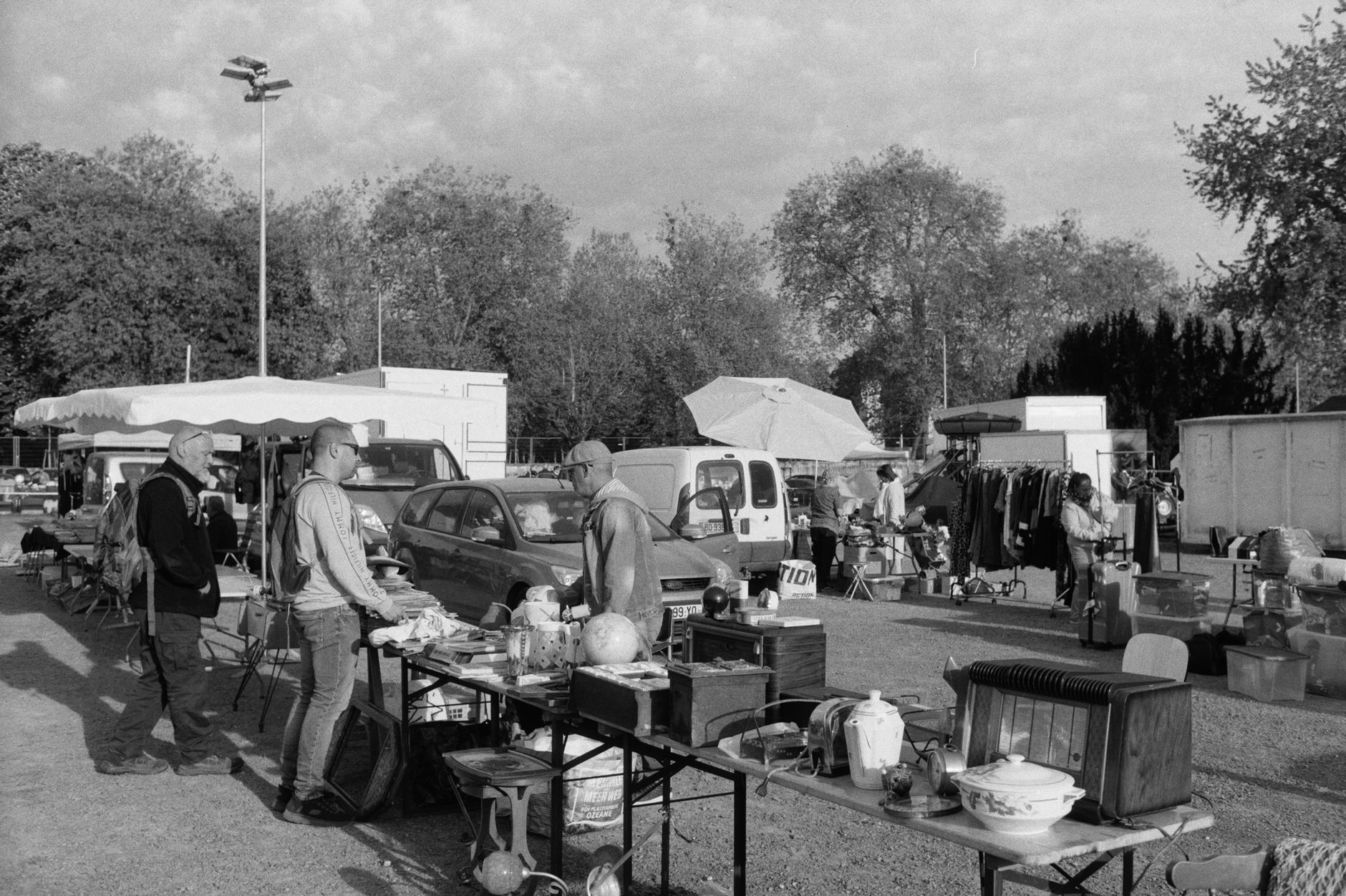 Black and white photo of a bustling outdoor flea market with stalls and shoppers.
