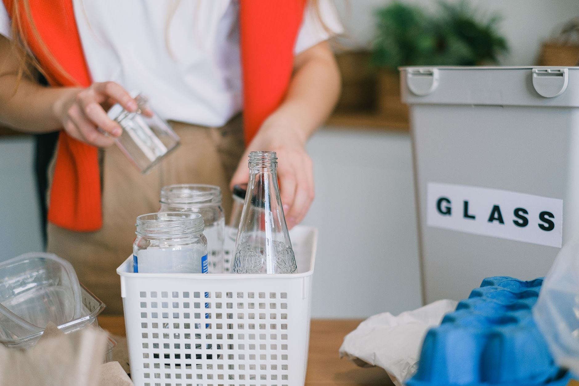 Crop anonymous female in casual clothes standing with reusable bottles and jars while sorting out rubbish for recycling in kitchen