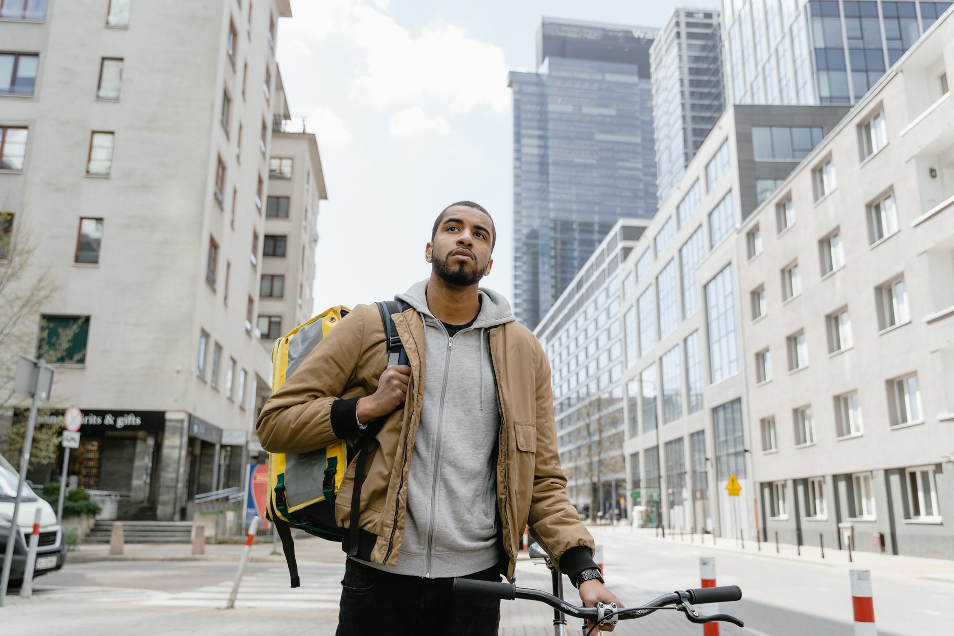 A cyclist stands outdoors with a backpack in a modern urban environment in Warsaw.