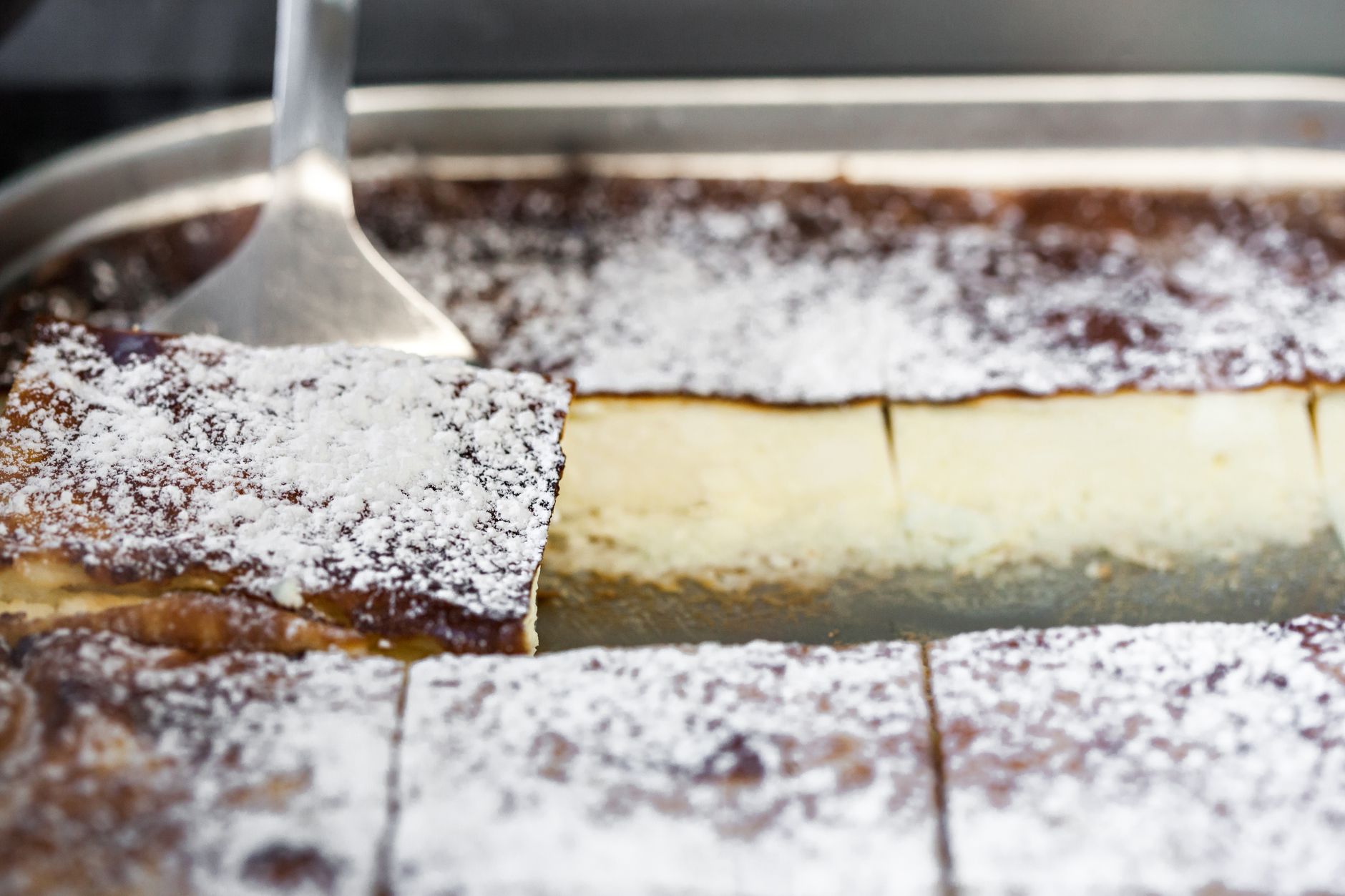 Delicious rectangular shaped cottage cheese dessert pieces with icing sugar in metal baking pan with spatula