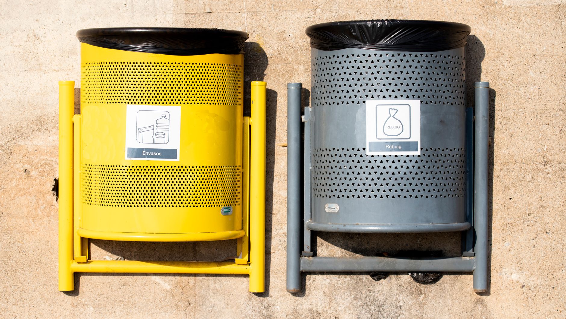 Bright yellow and gray recycling bins against a concrete wall in daylight.